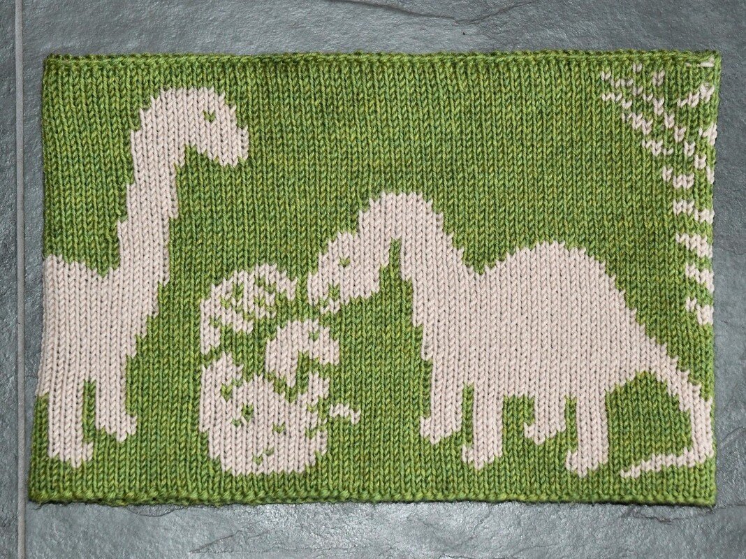 Knitted green panel with cream dinosaur silhouettes and small plant motifs, high-contrast children's design