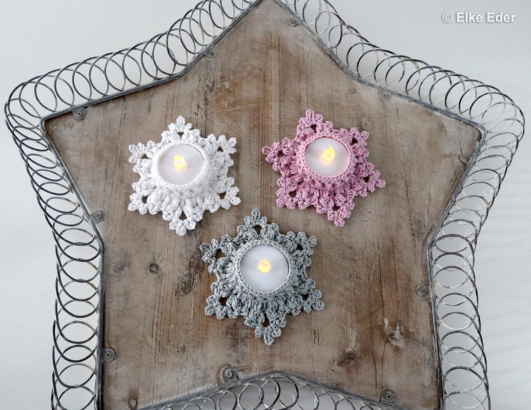 Three small crochet star tealight covers in white, pink and grey around LED tealights