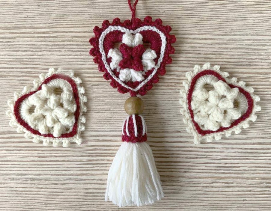 Drei gehäkelte Herzen in Rot und Creme, eines als Anhänger mit Holzperle und weißer Quaste