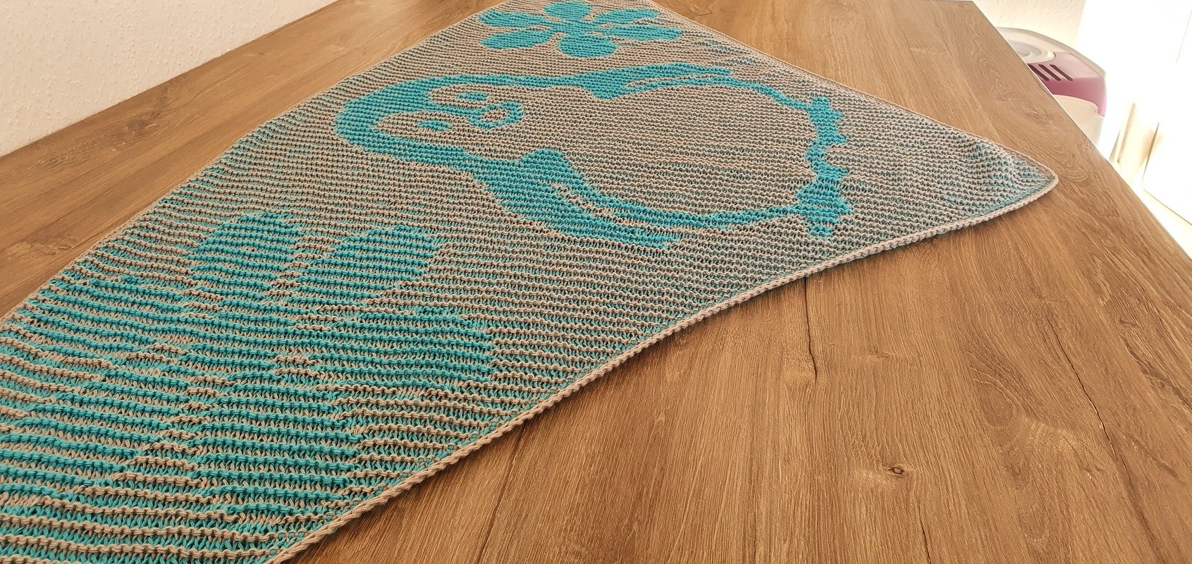 Gestricktes Dreieckstuch in Türkis und Hellgrau mit großen organischen Mustern, flach auf Holztisch