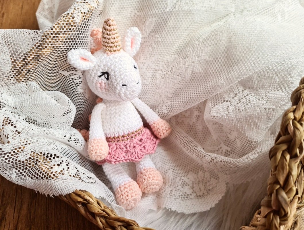 White crocheted unicorn amigurumi with pink skirt in a lace-lined basket