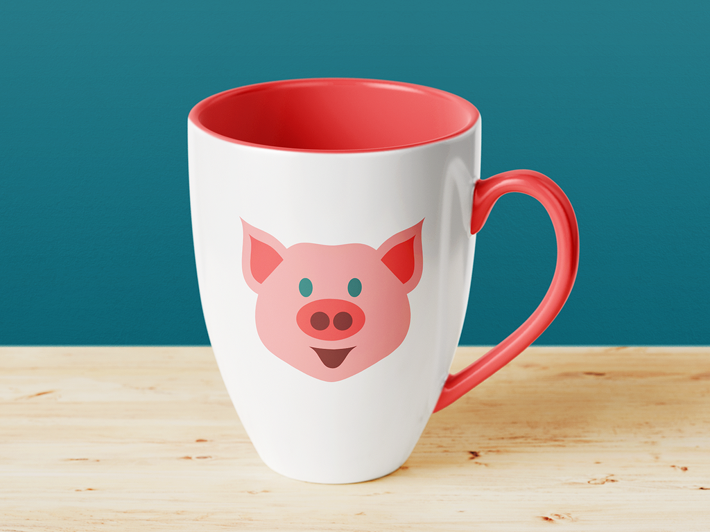 Weiße Tasse mit rotem Henkel und rotem Innenrand, rosa Schweinchen-Gesicht auf einem Holztisch