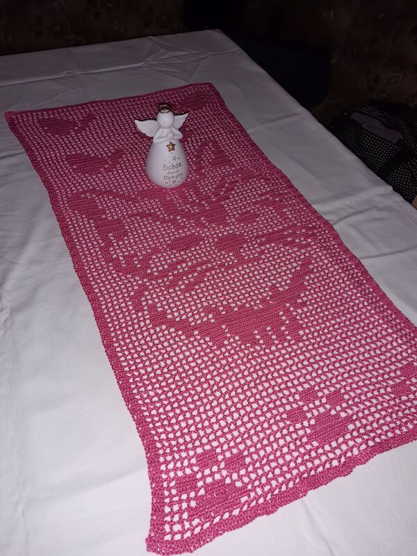 Rosa gehäkelter Filet‑Tischläufer mit Herzmuster auf weißer Unterlage, dekoriert mit kleiner Engel‑Figur