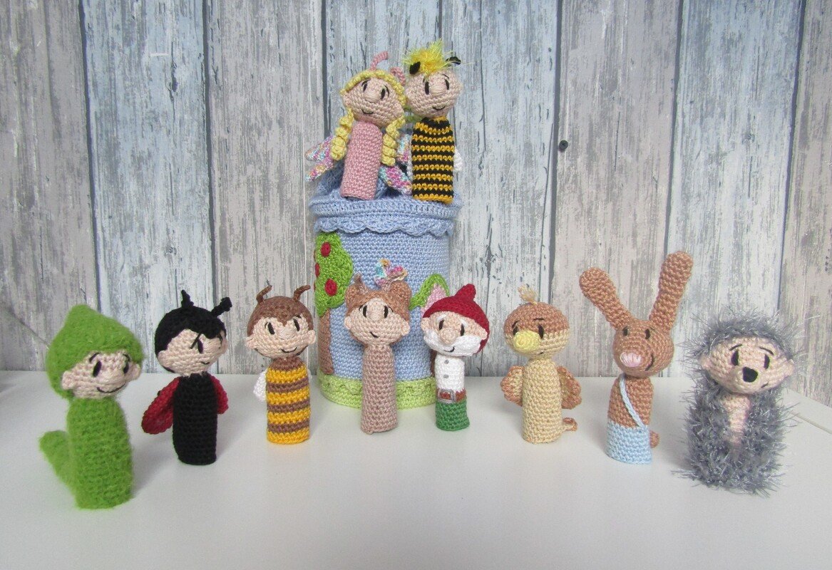 Mehrere bunte, handgehäkelte Fingerpuppen (Tiere und Märchenfiguren) vor hellem Holzpaneel.