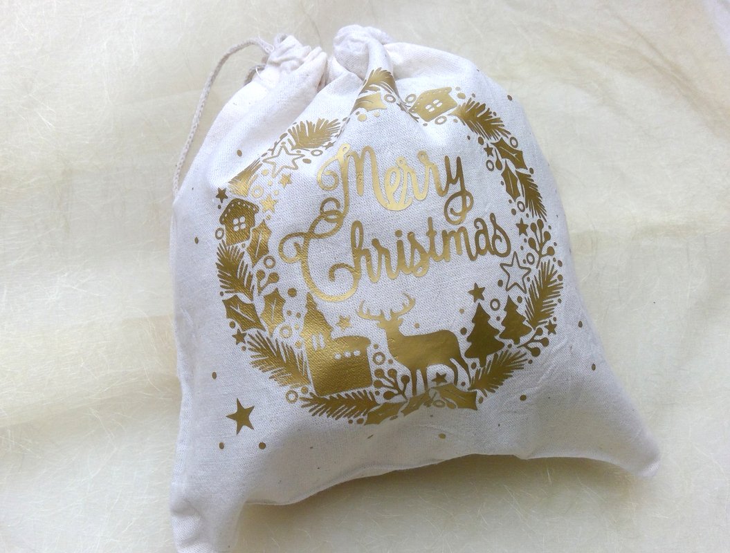 Heller Stoffbeutel mit goldfarbenem Kranzmotiv und ‚Merry Christmas‘-Schriftzug