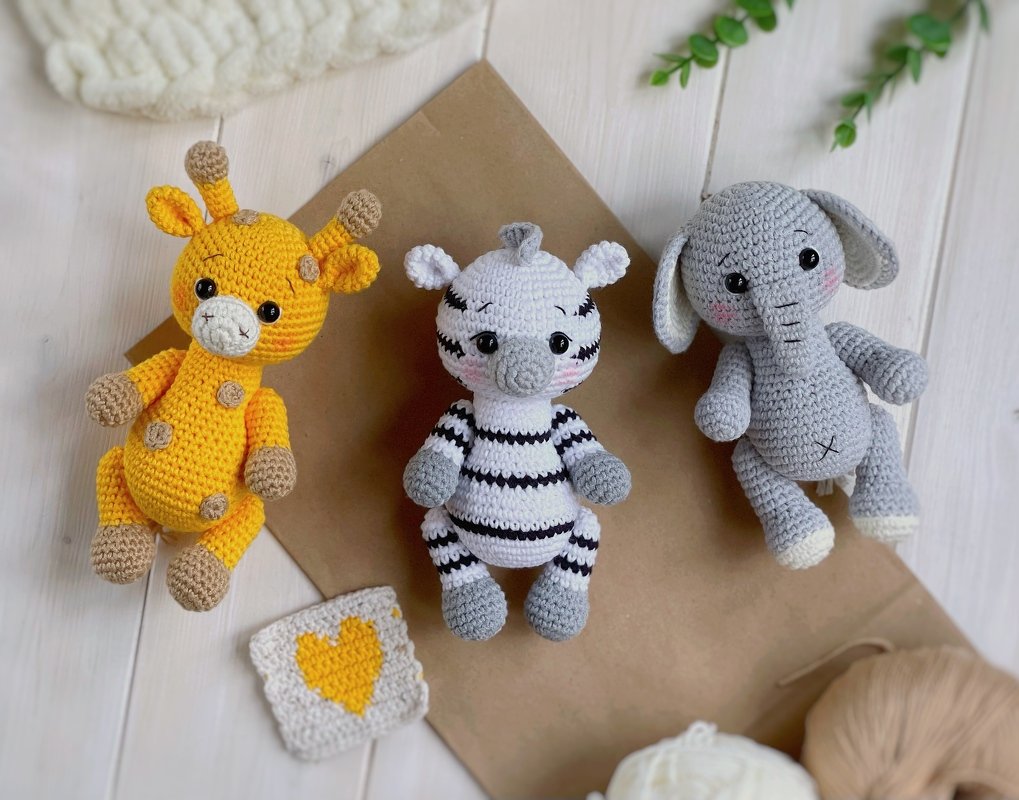 Gehäkelte Amigurumi-Giraffe, -Zebra und -Elefant auf hellem Holzhintergrund