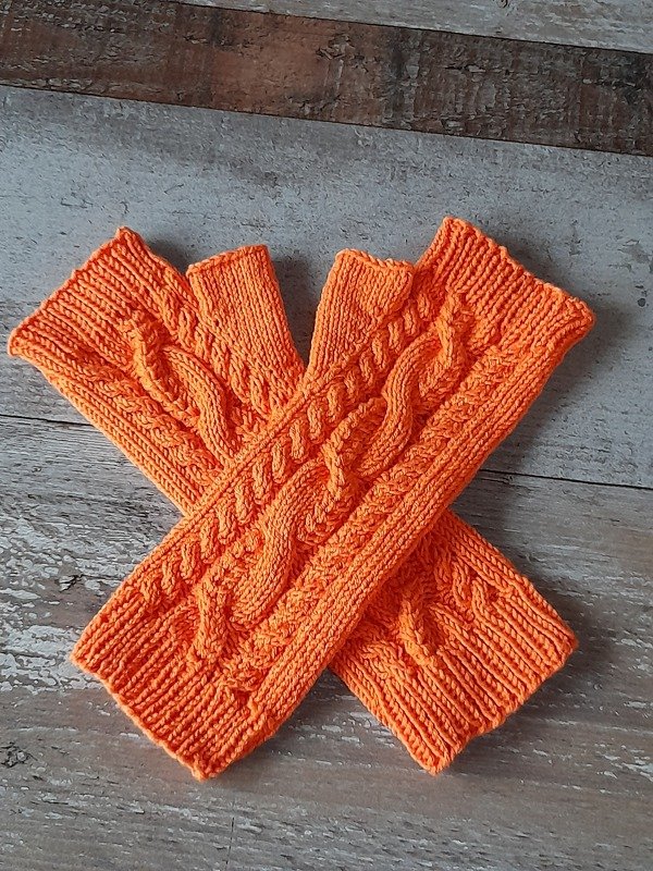 Oranges Paar gestrickter fingerloser Stulpen mit Zopfmuster auf Holzuntergrund