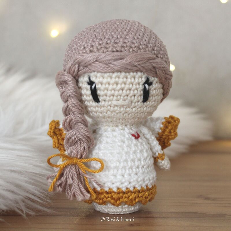 Gehäkeltes Engelchen-Amigurumi in Cremeweiß mit goldenen Flügeln und geflochtenem Zopf