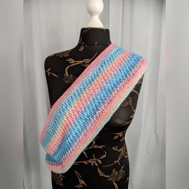 Gehäkelter Loop-Schal auf Schneiderpuppe mit horizontalen Pastellstreifen in Rosa, Hellblau und Mintgrün.