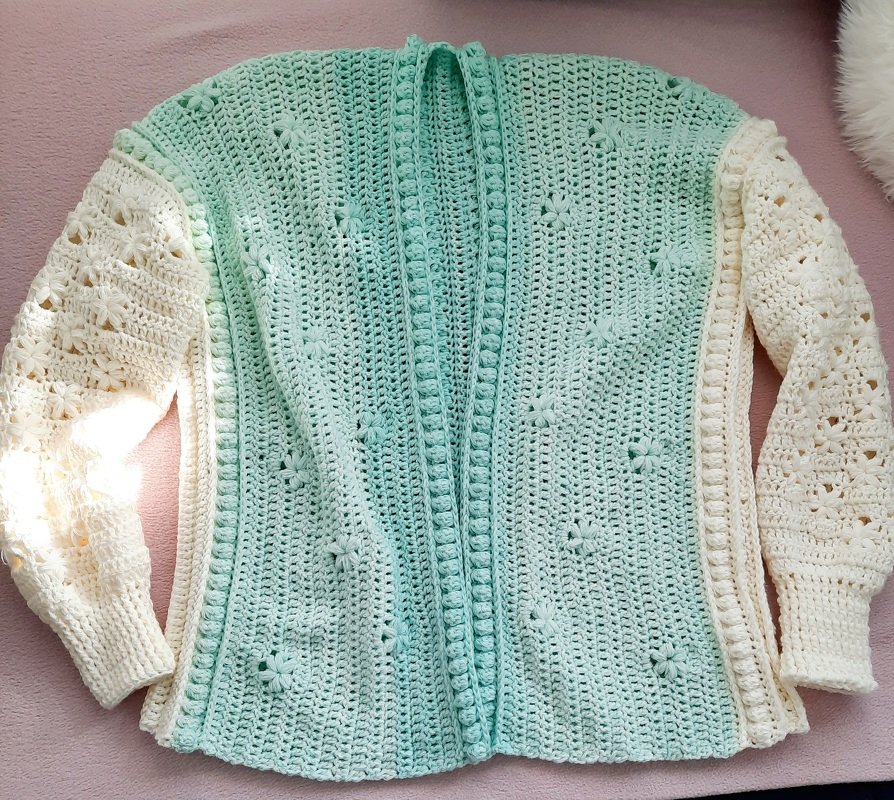 geöffnete gehäkelte Damenjacke liegend in Mint mit cremefarbenen, ajour gehäkelten Ärmeln