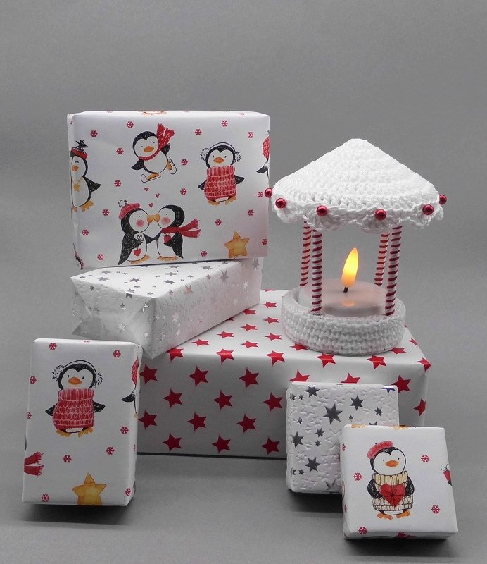 Weihnachtsgeschenke mit Pinguin- und Sternenpapier neben einer gehäkelten LED-Laterne