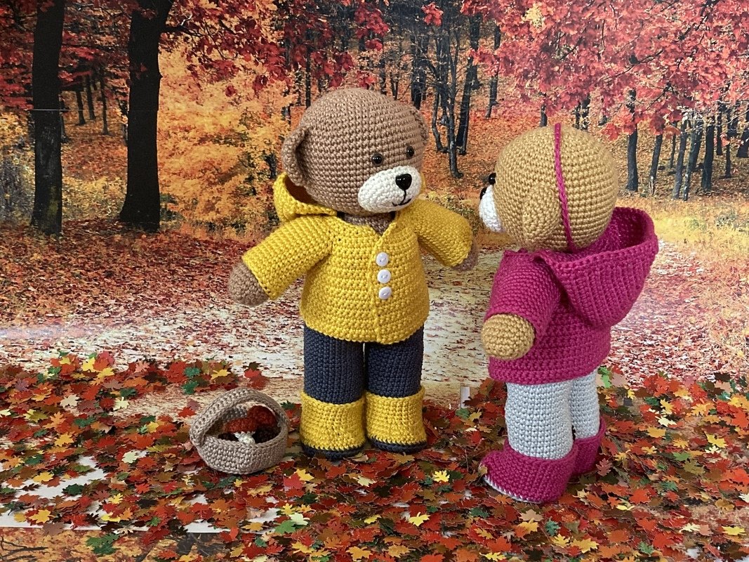 Zwei Amigurumi-Teddys mit Kapuzenjacken und Stiefeln sowie einem Korb im Herbstlaub