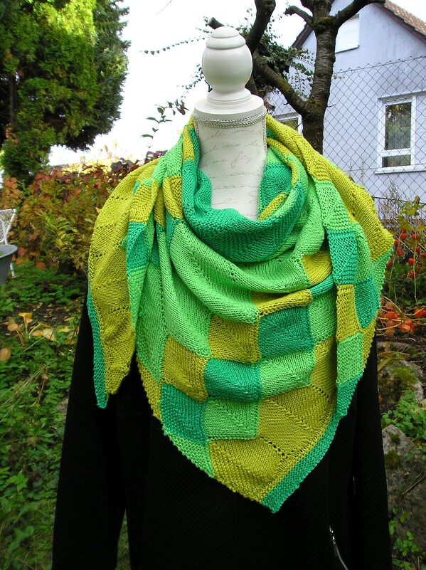 Grünes gestricktes Dreieckstuch mit quadratischem Blockmuster und Lochdetails auf einer Schaufensterpuppe.