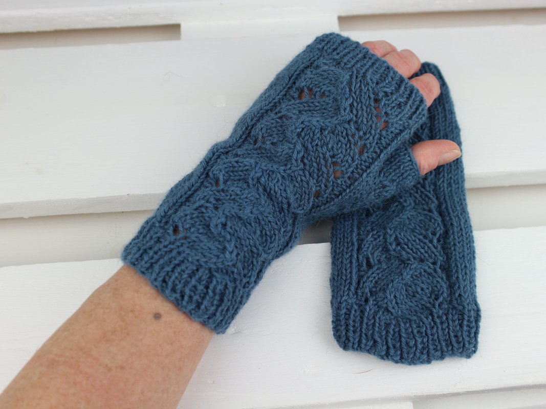 Petrolblaue, gestrickte Armstulpen mit Zopfmuster und Lochdetails, getragen vor hellem Hintergrund.