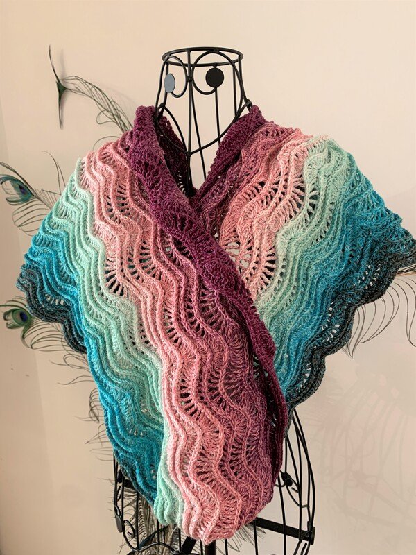 Crochet wave lace scarf draped on a wire dress form with gradient colors from burgundy to teal