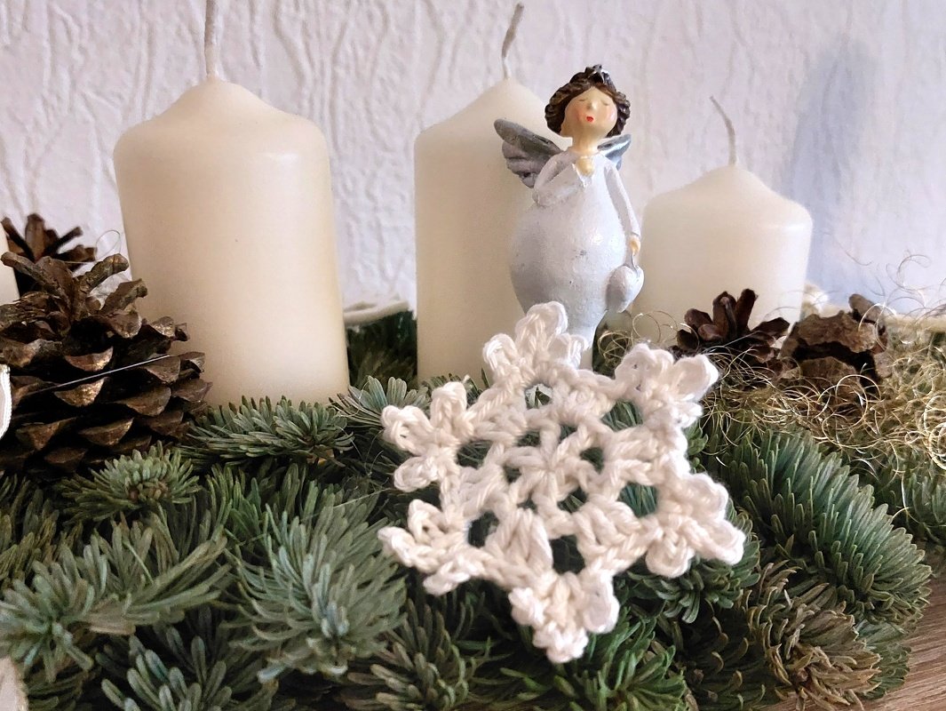Weiße, schnell gehäkelte Schneeflocke auf einem Adventskranz aus Tannengrün neben Kerzen und Zapfen