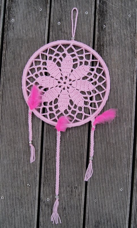 Rosa gehäkelter Traumfänger mit Blumen‑Mandala, drei geflochtenen Bändern, pinken Federn und Perlen vor Holzlatten