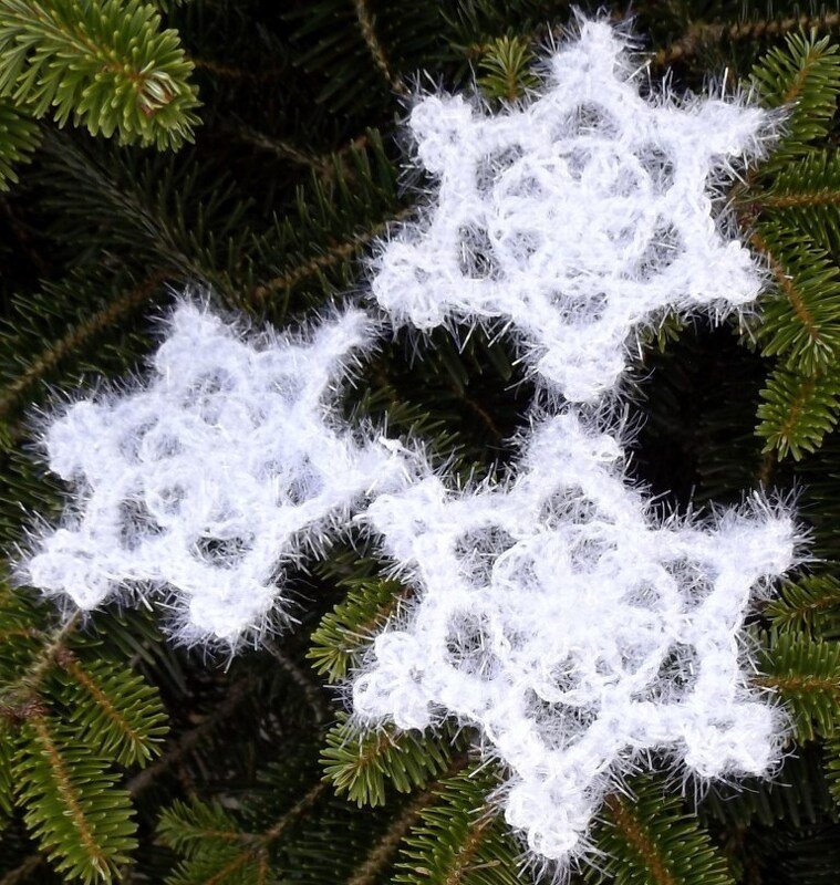 Drei weiße, flauschige Schneeflocken aus Häkelgarn auf grünen Nadelbaumzweigen