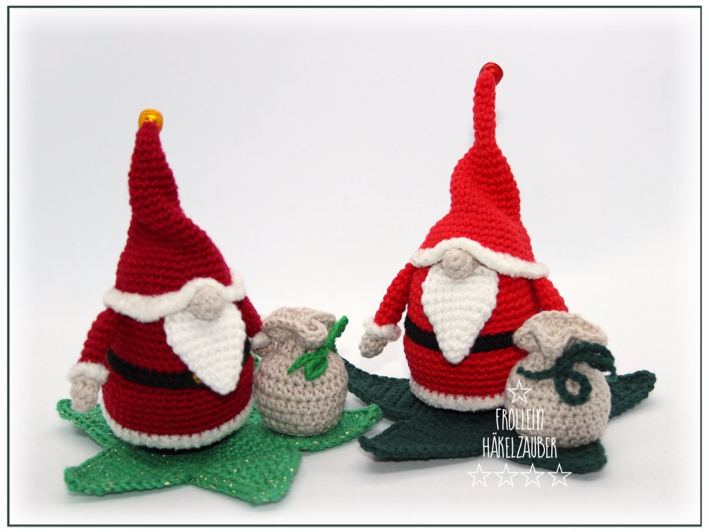 Zwei gehäkelte rote Wichtel mit weißen Bärten und Zipfelmützen auf grünen Sternen, mit kleinen beigen Säckchen