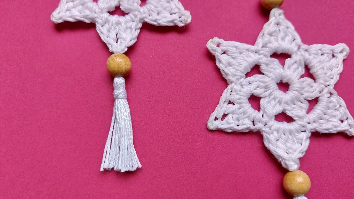 Detailed view of crochet star stitch pattern with wooden bead and white tassel on pink background