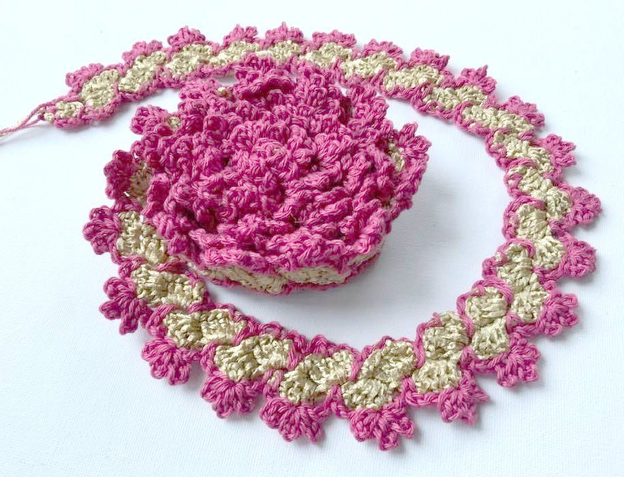 Gehäkelte Dekoration in Rosa und Beige auf weißem Hintergrund