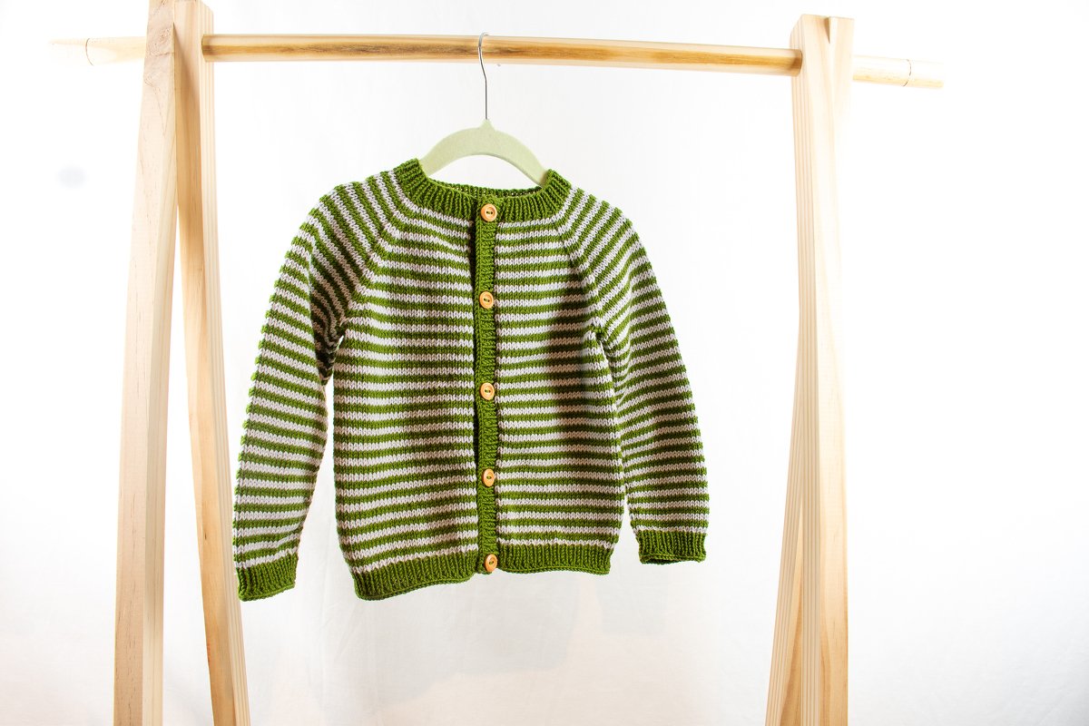 Grün-weiß gestreifte Kinderstrickjacke mit Holzknöpfen an einem Holzständer