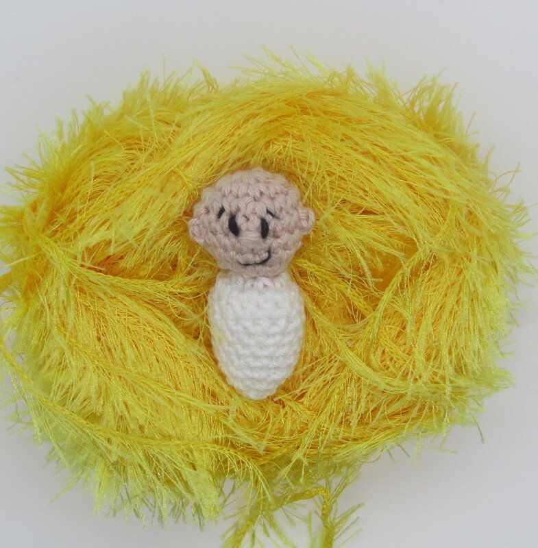Gehäkelte Mini-Amigurumi-Fingerpuppe mit beigem Kopf und weißem Körper im flauschigen gelben Garnnest