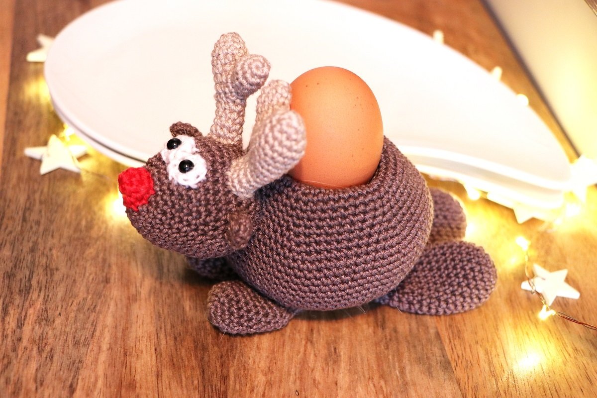 Gehäkeltes Rentier mit roter Nase als Eierhalter neben Lichterkette