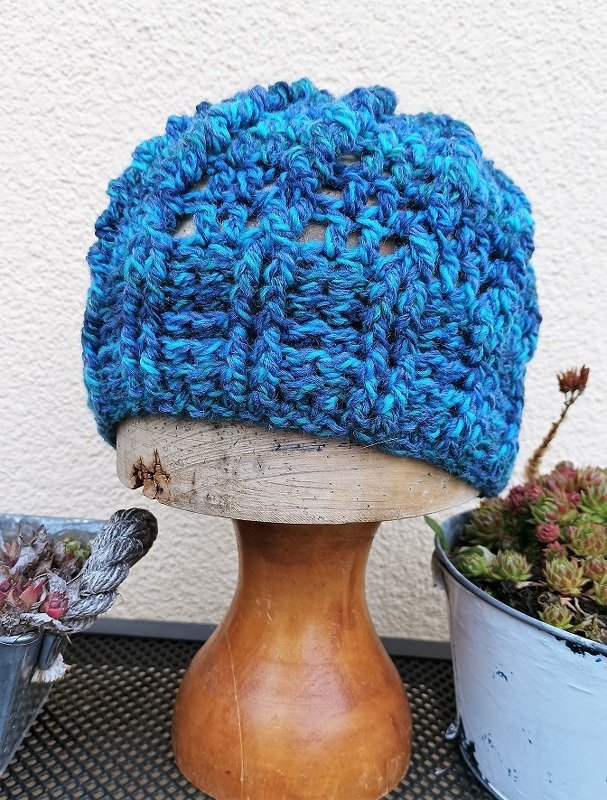 Handgehäkelte Mütze in Blau- und Türkistönen auf einem Holzständer