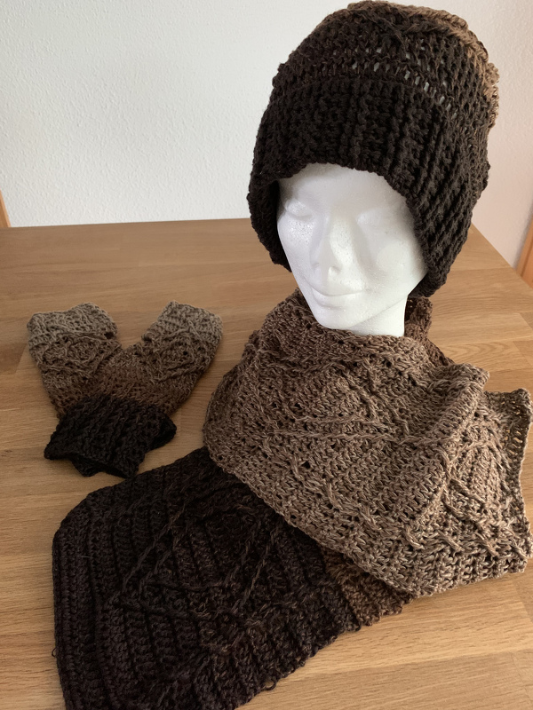 Gehäkeltes dreiteiliges Damen-Set mit Mütze auf einem Kopfmodell, Schal und Stulpen in Braun-Farbverlauf auf Holzoberfläche