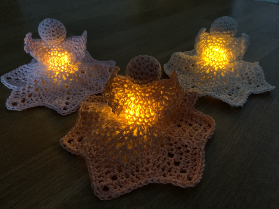 Drei leuchtende, gehäkelte Engel in Weiß und Rosa auf dunklem Holz