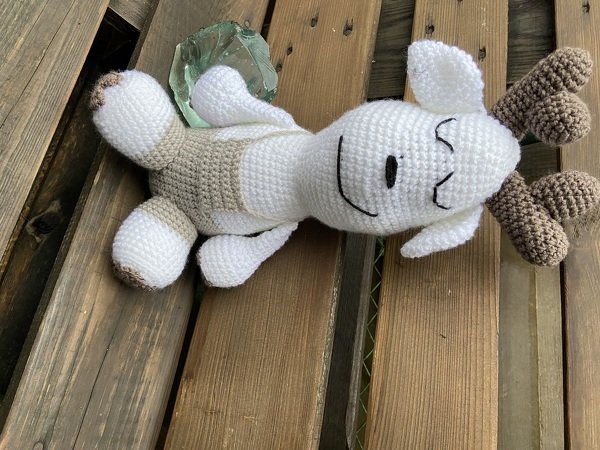 Rentier-Amigurumi aus weißem und braunem Garn liegend auf Holzbrett