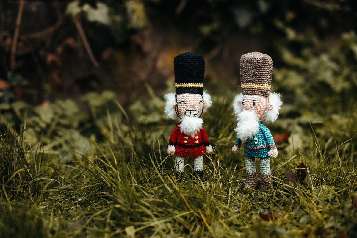 Zwei gehäkelte Amigurumi-Nussknacker in roten und türkisfarbenen Uniformen auf Gras