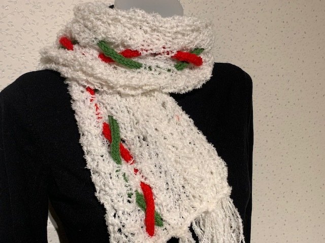 Weißer gestrickter Schal mit roten und grünen Akzenten über schwarzem Oberteil