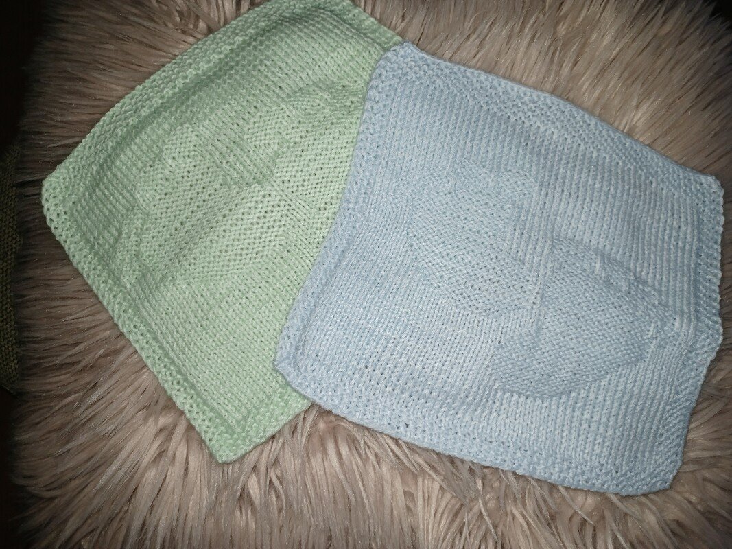 Zwei gestrickte Quadrate in Pastellgrün und Pastellblau mit erhabenem Herzmuster auf flauschigem Untergrund