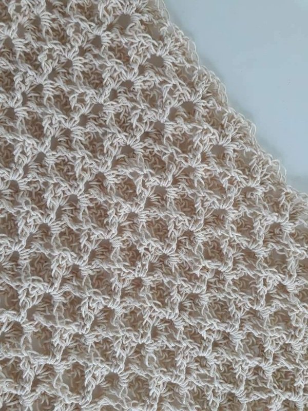 Nahaufnahme eines cremefarbenen, gehäkelten Spitzentuchs mit filigranem Sternenmuster und offener Struktur.