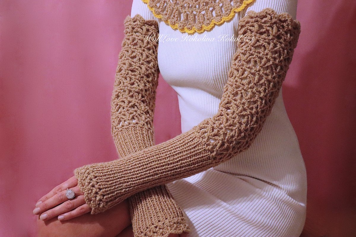 Beige, gehäkelte Armstulpen mit Lochmuster und Rippenbündchen, getragen über einem weißen Oberteil vor rosa Hintergrund