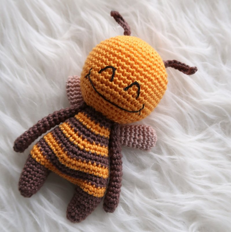 Gehäkelte Amigurumi-Biene mit gesticktem Lächeln auf weißem, flauschigem Untergrund