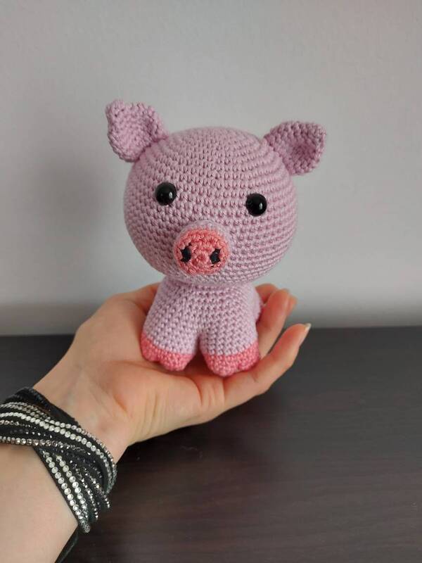 Hand hält kleines rosa gehäkeltes Schweinchen mit dunklen Augen und etwas dunklerer Schnauze