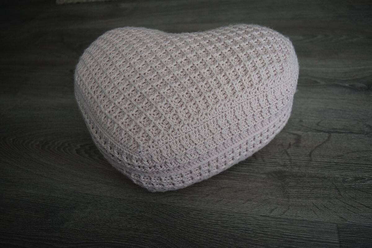 Gehäkeltes Herzkissen in zartem Rosé mit Waffelmuster auf dunklem Holzfußboden