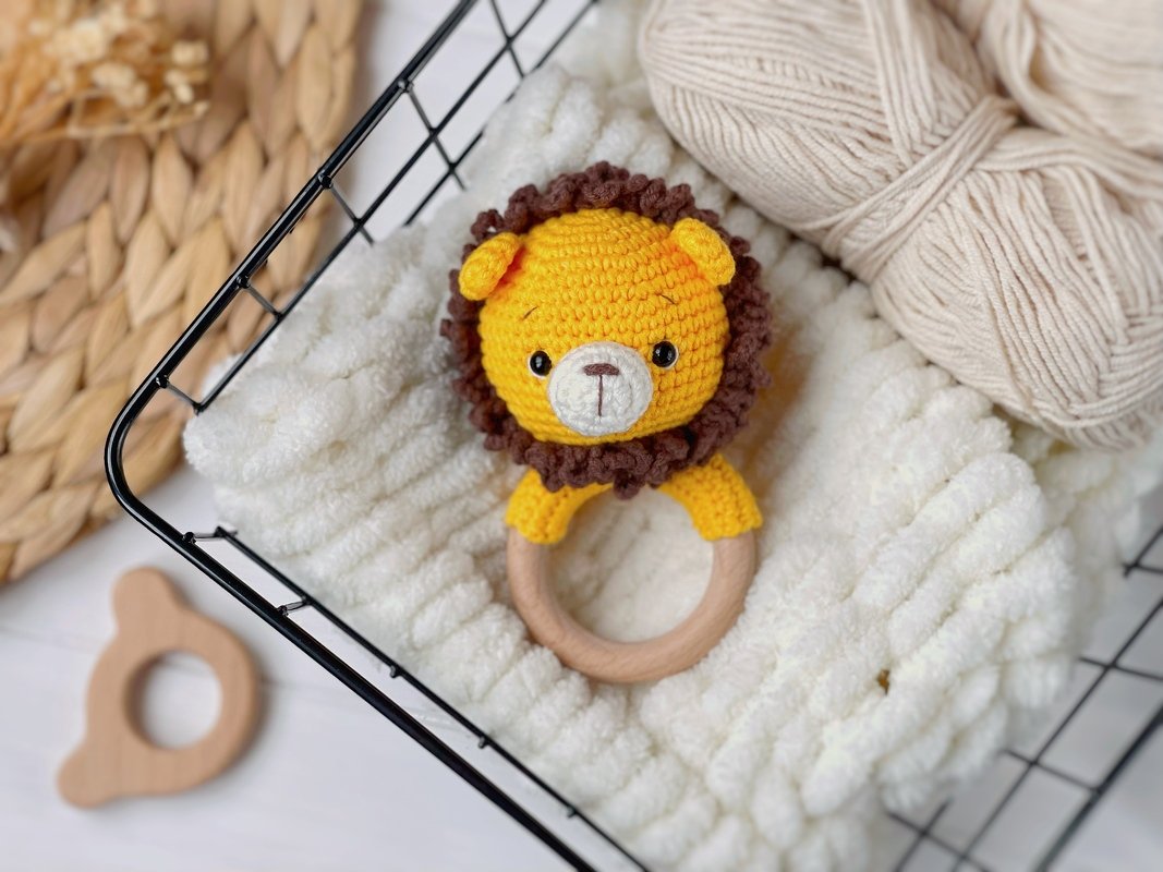 Yellow crocheted lion rattle attached to a wooden ring on a white textured blanket