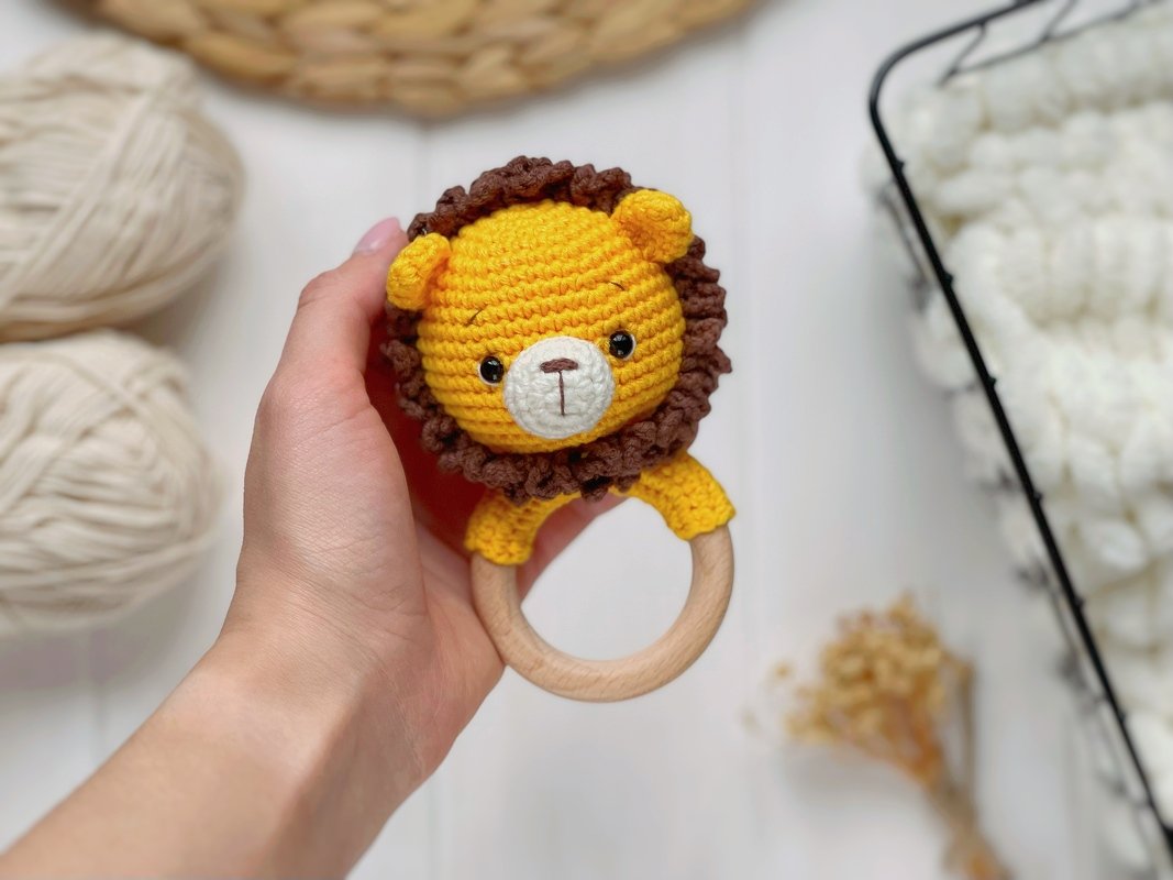 Hand holding a crocheted yellow lion teether with a wooden ring