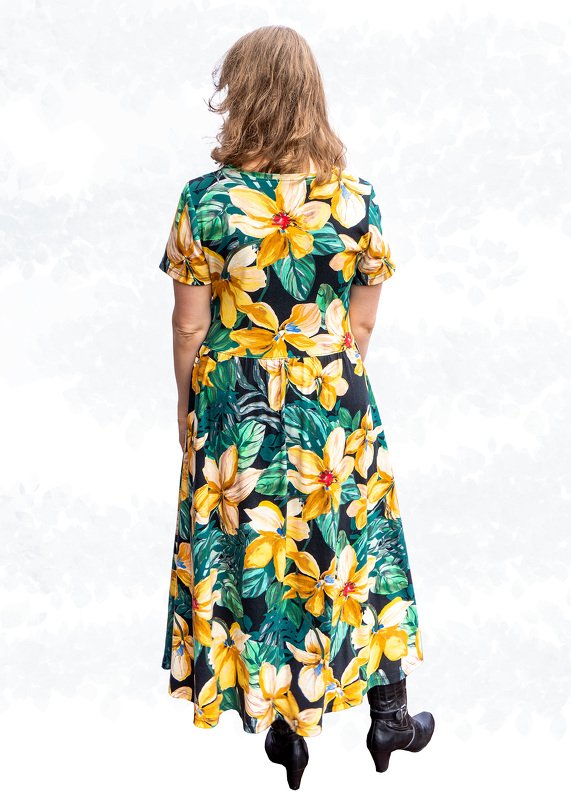 Rückenansicht einer Trägerin in einem knöchellangen Kleid mit großen gelben Blüten und grünen Blättern; kurze Ärmel und betonte Taille.