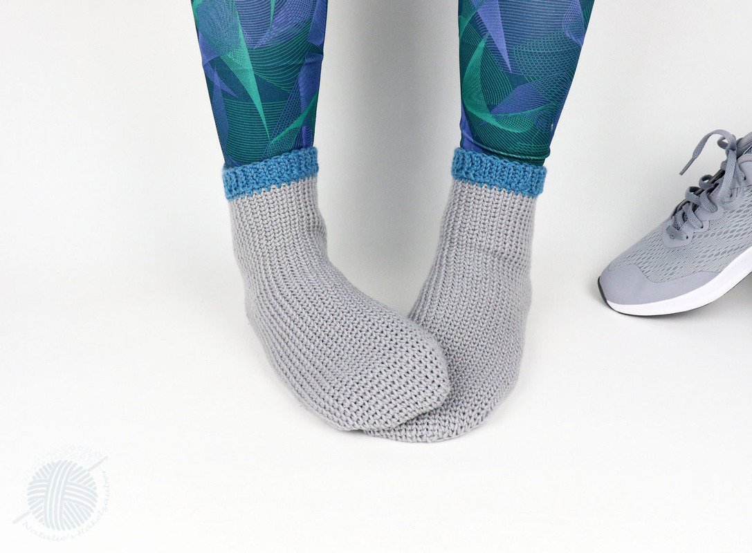 Close-up of grey crocheted ankle socks with blue cuff beside gray athletic shoe