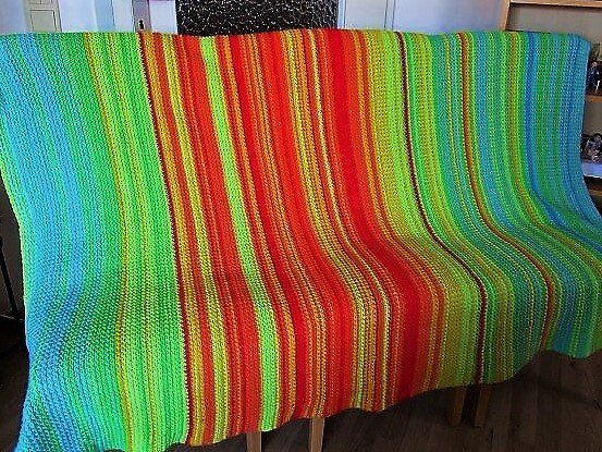 Gehäkelte Decke mit vertikalen Streifen in leuchtenden Blau-, Grün-, Gelb-, Orange- und Rottönen.