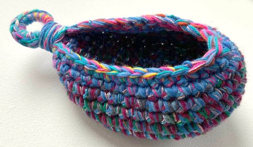 Gehäkelter kleiner bunter Korb mit Schlaufe auf hellem Hintergrund