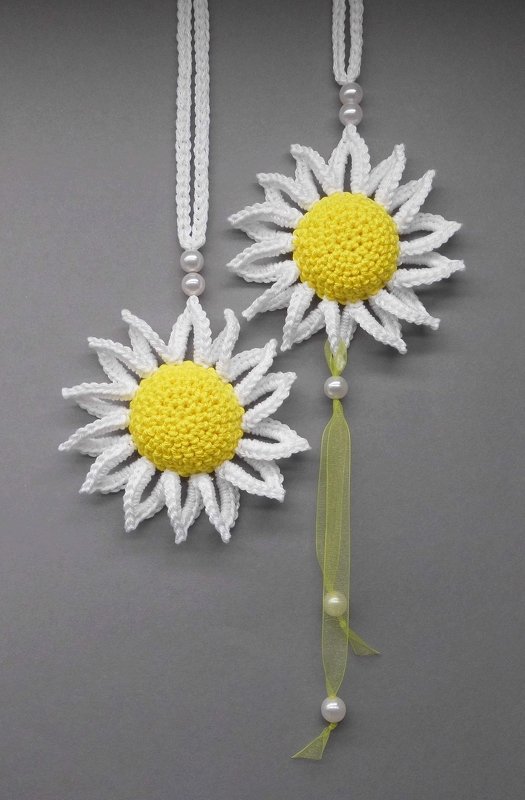 Häkelanhänger in Blumenform mit gelbem Zentrum, weißen gezackten Blütenblättern, Perlen und grünem Organza-Band