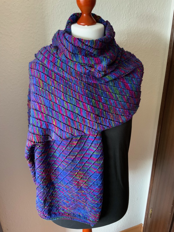 Gestrickter, mehrfarbiger Schal mit diagonalen Streifen in Blau, Pink und Grün auf einer Schneiderpuppe.