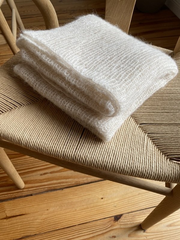 Detail of a folded cream textured knit scarf on a wooden woven chair seat