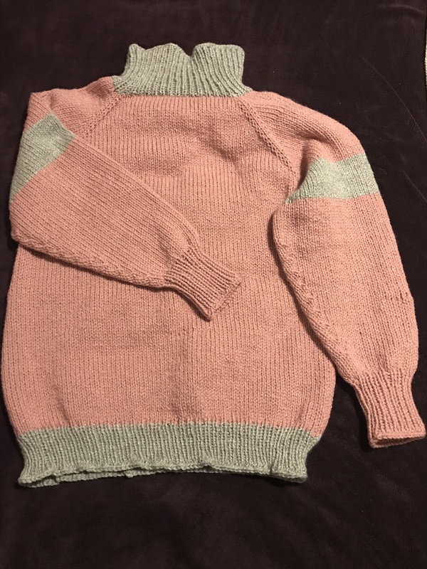 rosa-grauer gestrickter Damenpullover mit Stehkragen, Raglanärmeln und gerippten Bündchen, flach auf dunklem Untergrund liegend
